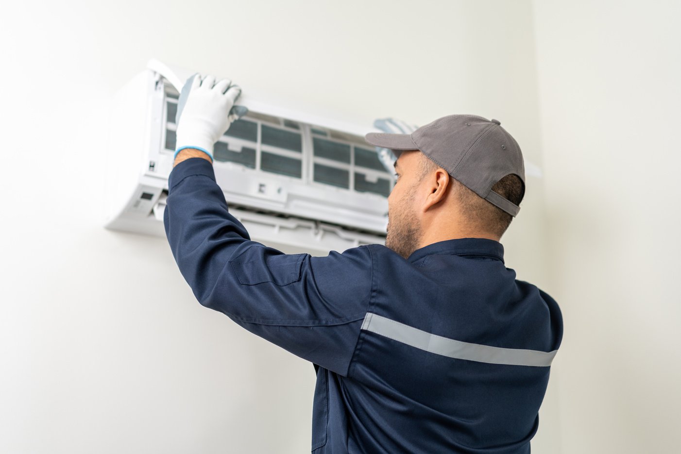 Air conditioner service indoors. Air conditioner cleaning technician He opened the front cover and took out the filters and washed it. He in uniform wearing rubber